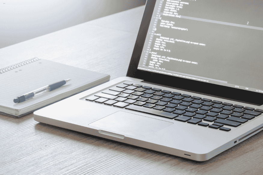 Notebook aberto com tela exibindo código e caderno ao lado sobre mesa